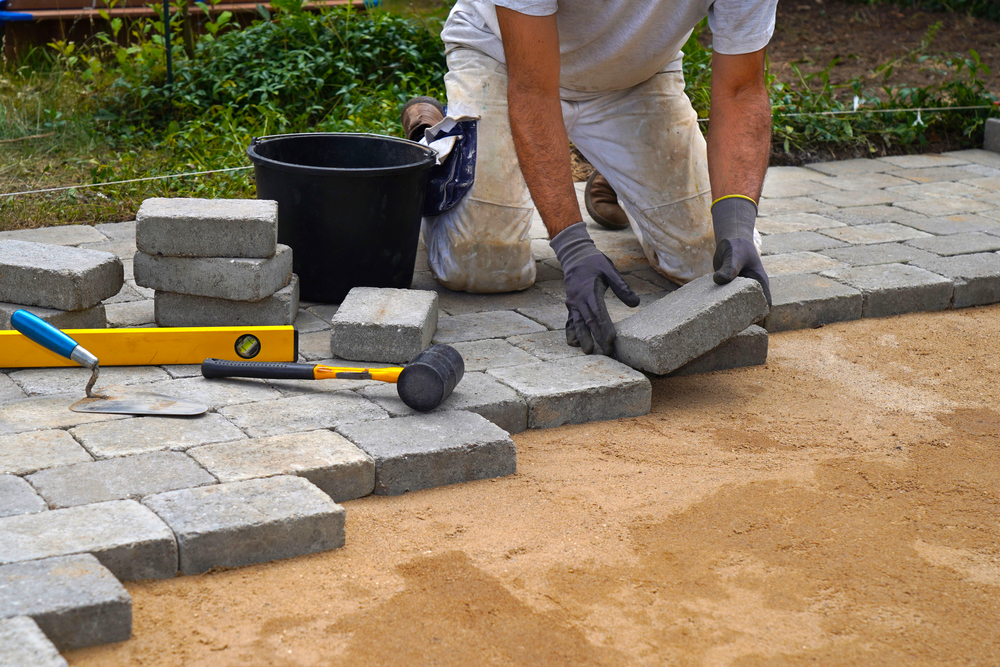 craftsman lays concrete paving stone blocks on sand