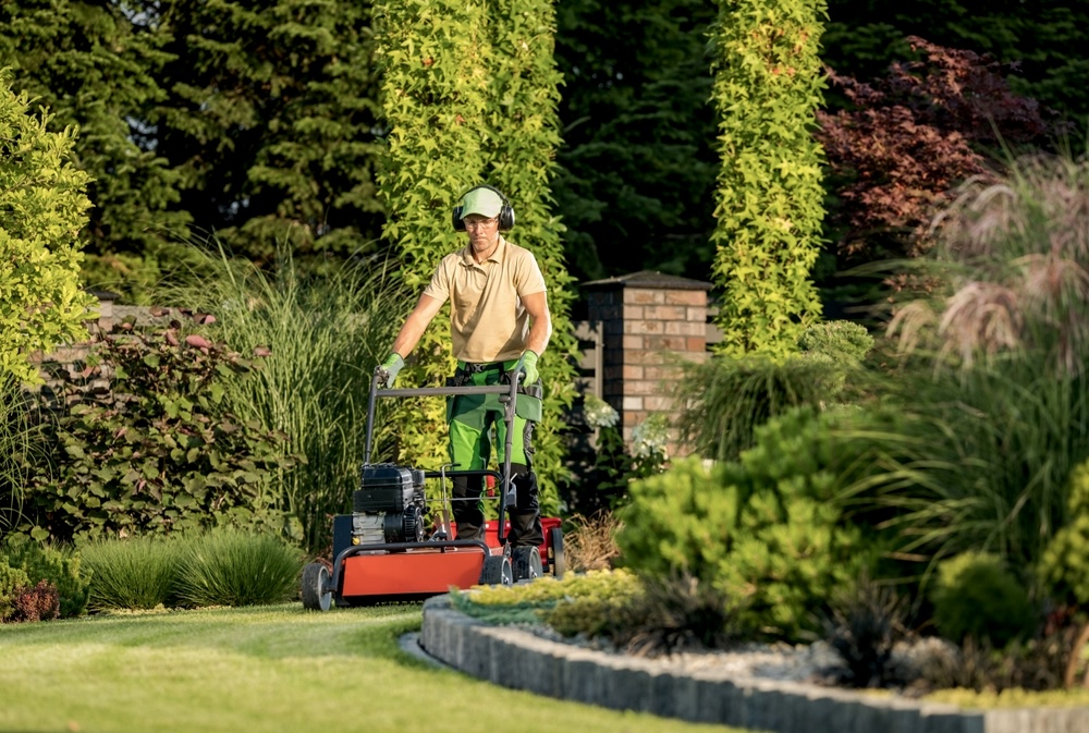 A gardener wearing a yellow shirt mowing the green lawn